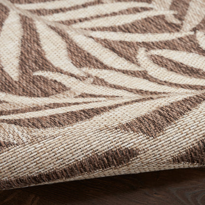 Beige and brown woven rug with geometric leaf pattern, textured fabric, folded edge on dark wood floor.