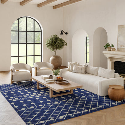 Bright living room with beige sofa, curved cream chairs, wood beam ceiling, navy geometric rug, light wood coffee table.