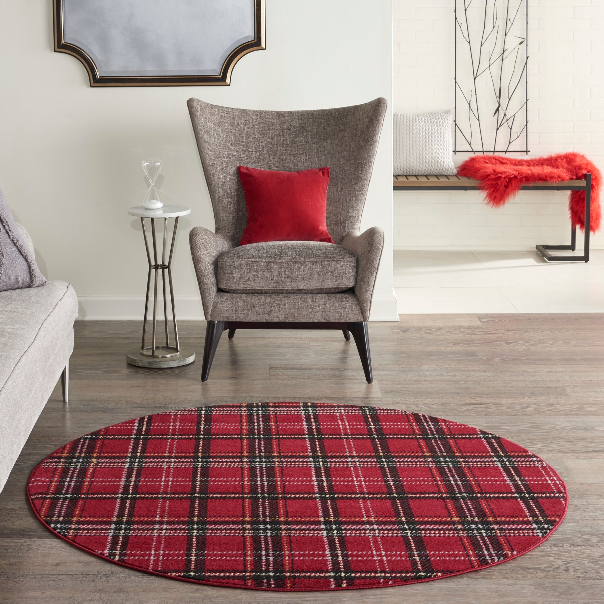Round red plaid rug on wood floor with gray upholstered armchair and red cushion in a modern living room.