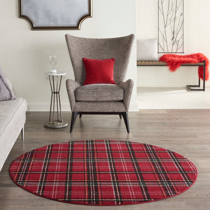 Round red plaid rug on wood floor with gray upholstered armchair and red cushion in a modern living room.