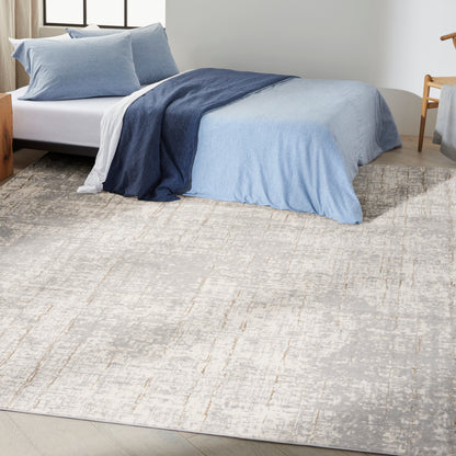Light beige abstract-patterned area rug (8' x 10') on the floor, with a low-profile bed & blue gradient quilted bedding visible nearby.