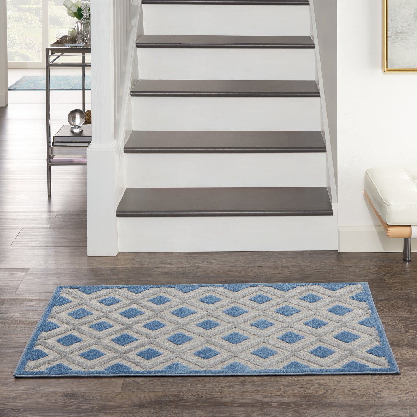 Blue and white geometric lattice rug (3' x 4') in front of a white staircase with dark wood treads on a dark wood floor.