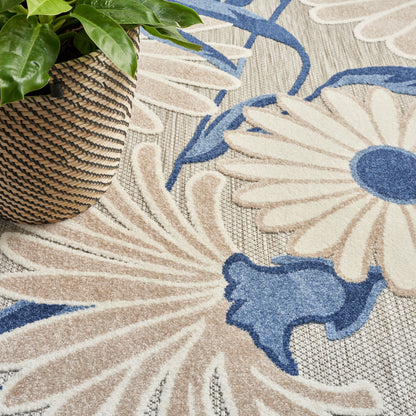 Woven wicker plant basket with green leafy plant on a beige and blue floral patterned rug.