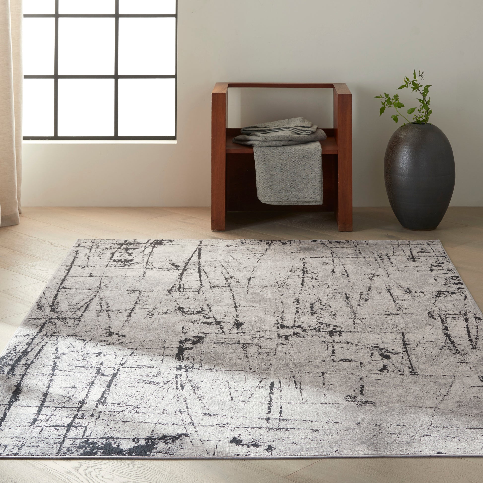 Abstract gray area rug with black linear pattern in a bright living room, paired with a wooden side table and gray vase.