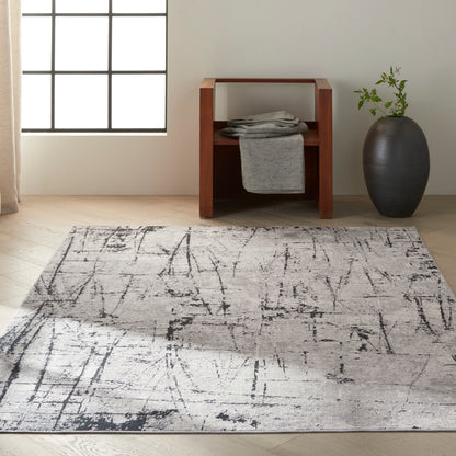 Abstract gray area rug with black linear pattern in a bright living room, paired with a wooden side table and gray vase.
