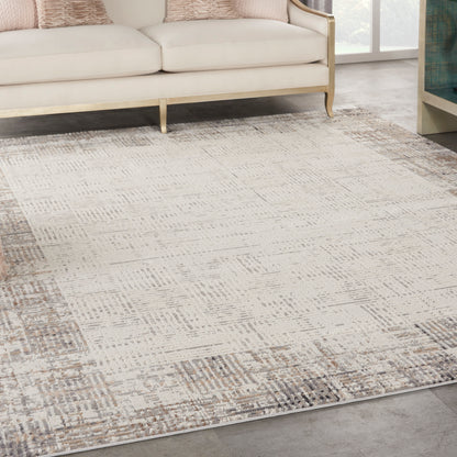 Neutral geometric area rug in cream, beige and taupe tones under a cream sofa with gold legs.