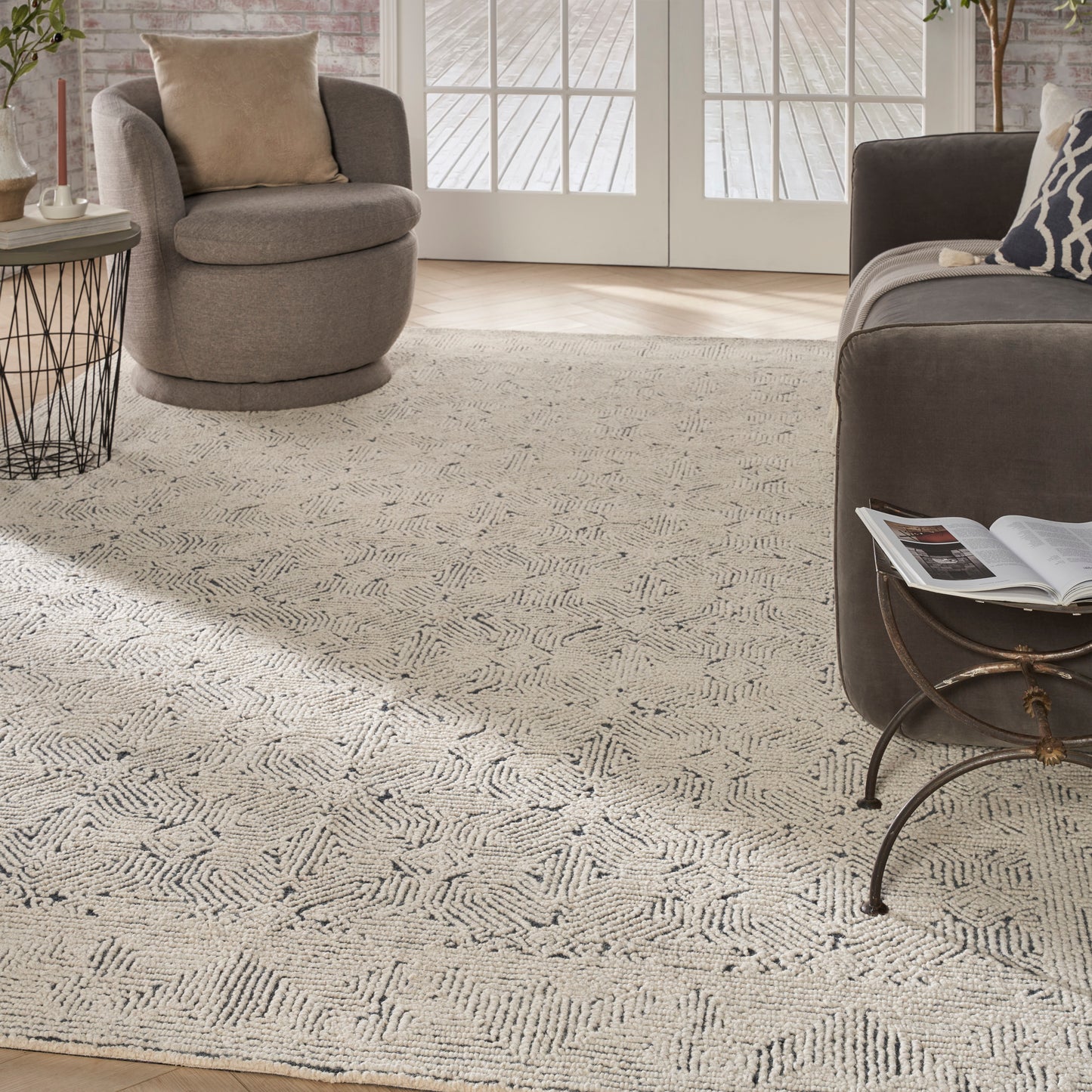 Neutral beige looped-pile area rug with geometric chevron pattern, gray rounded armchair, dark sofa, glass doors.