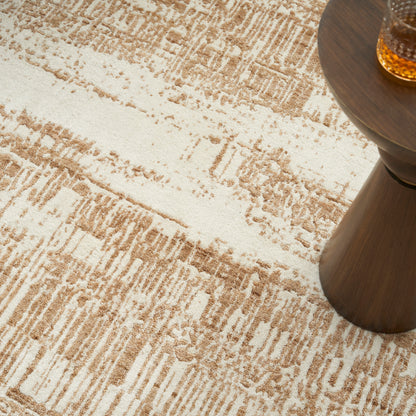 Beige patterned rug in cream and tan tones beside a dark wood round side table with a glass of amber liquid.