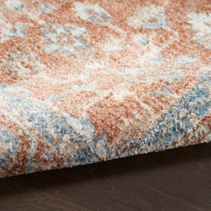 Close-up of a plush patterned area rug in peach, blue and ivory tones, edge folded over a dark wood floor.