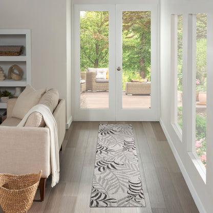 Long gray leaf-patterned rug runner on wooden floor in a bright beige living room with a beige sofa and wicker basket.