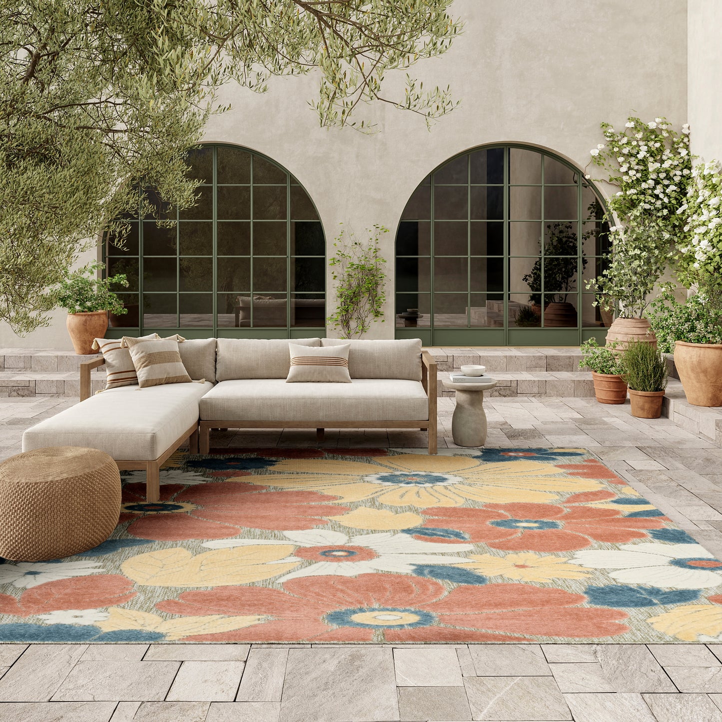 Mediterranean courtyard with arched windows, beige sectional sofa on wood frame, colorful floral rug, potted plants.
