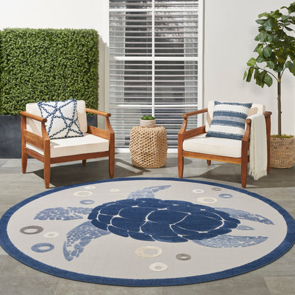 Round blue outdoor rug with a sea turtle motif; two wooden chairs with white cushions and blue pillows on a patio.