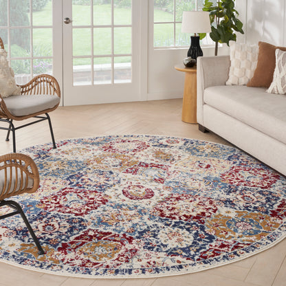 Round multicolor Persian-style area rug in cream, red, blue and gold; beige sofa, rattan chairs in a bright living room.