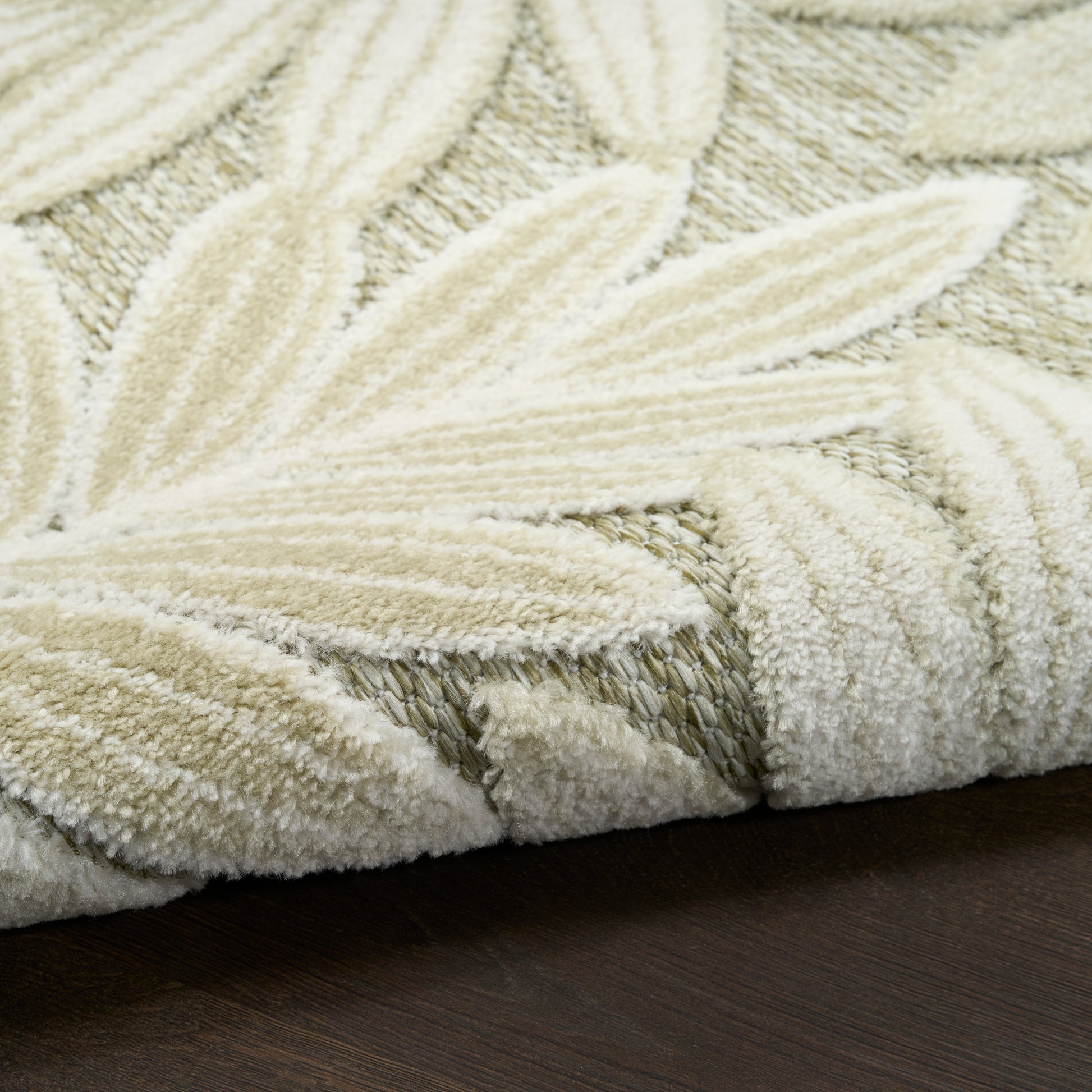 Cream looped-pile rug with leaf-pattern motifs and plush texture on dark wood floor.