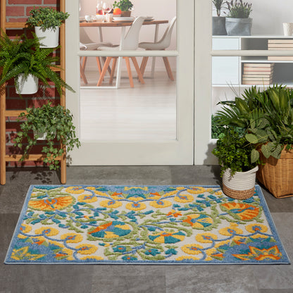 Rectangular colorful floral outdoor doormat with blue border; entryway with potted plants and glass door to a dining room.