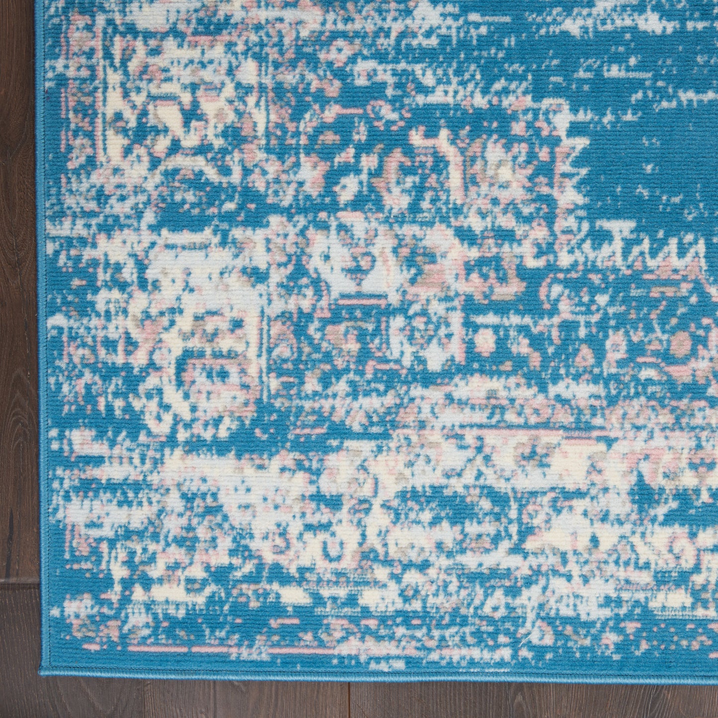 Turquoise blue distressed pattern rug with pink and ivory accents and a border, on wood floor.