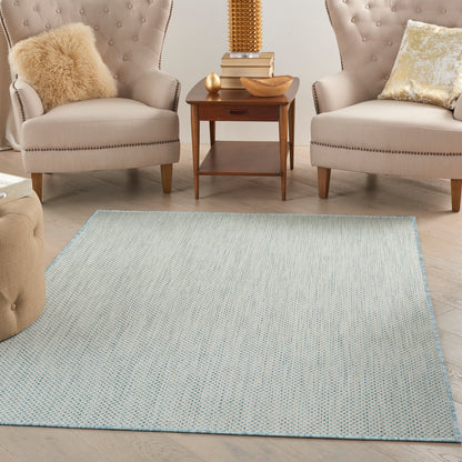 Two beige tufted armchairs with nailhead trim flank a wooden end table on a pale blue woven rug.