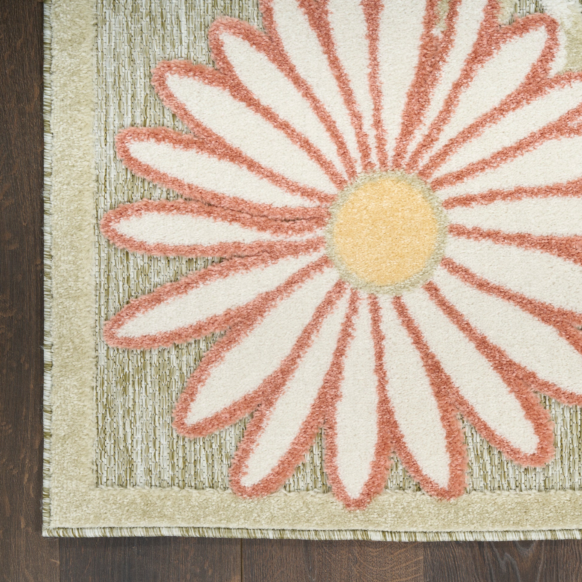 Close-up of a cream rug featuring a large pink-outlined daisy with a yellow center, beige border, on dark wood floor.