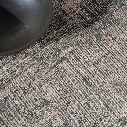 Gray and cream geometric patterned rug with chevron texture; dark round planter sits in the top-left.