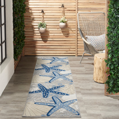 Coastal blue starfish runner rug on a light wooden patio with wicker chair & hanging planters.
