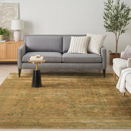 Grey fabric sofa with two cushions, round wood-top coffee table, olive-toned rug, potted plant in a modern living room.