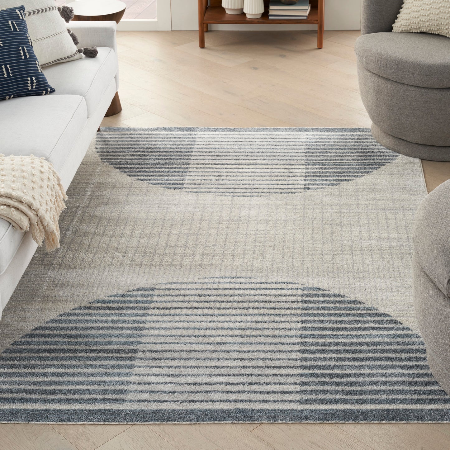 Rectangular gray rug with navy blue curved arcs and stripes; modern living room with light wood floor and neutral seating, 7' x 9'.