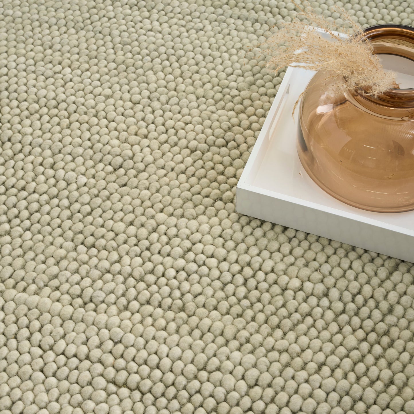Beige loop-pile rug with a round amber glass vase on a white tray tied with a burlap ribbon