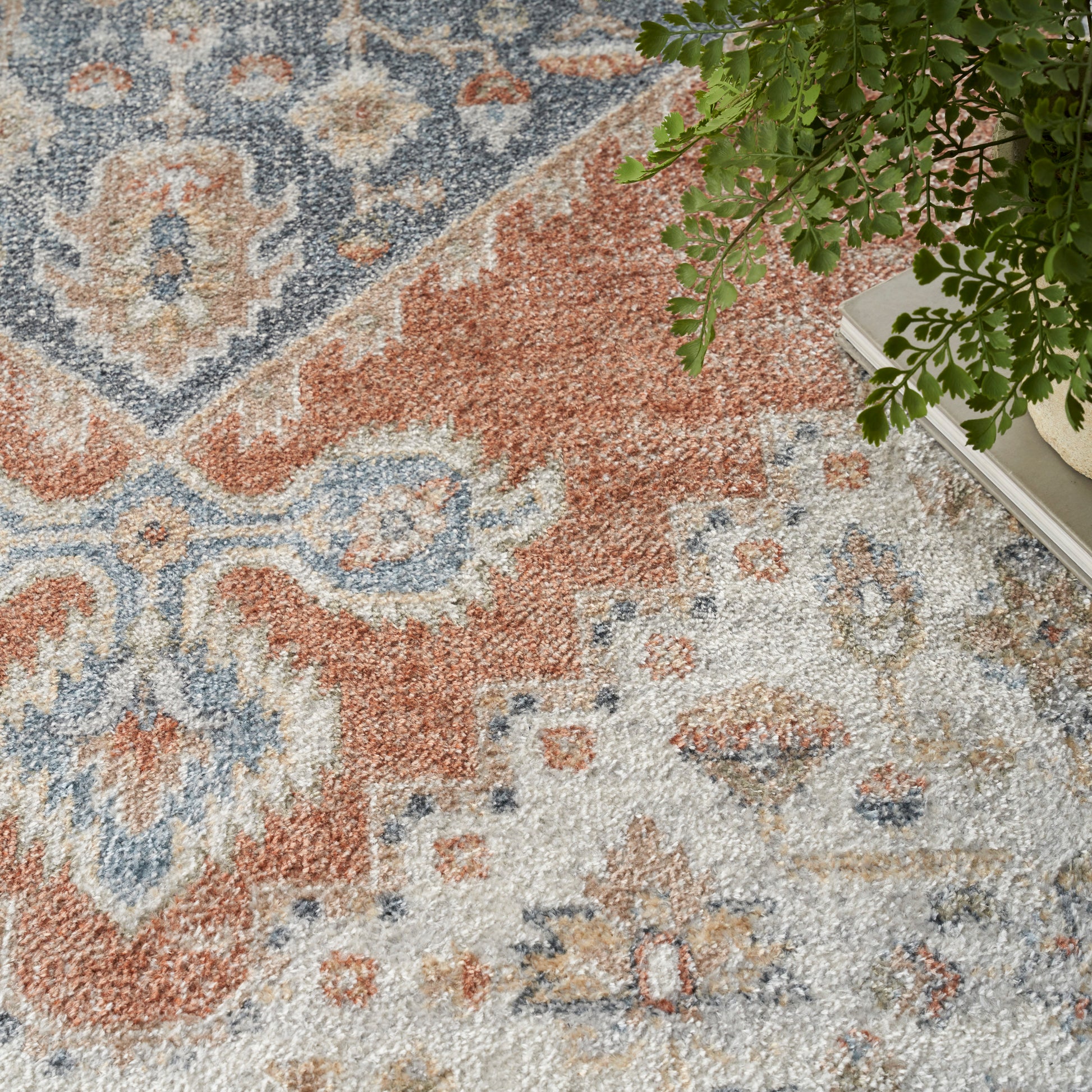 Rust, blue, and cream oriental rug with floral motifs; plush pile beside a potted plant.