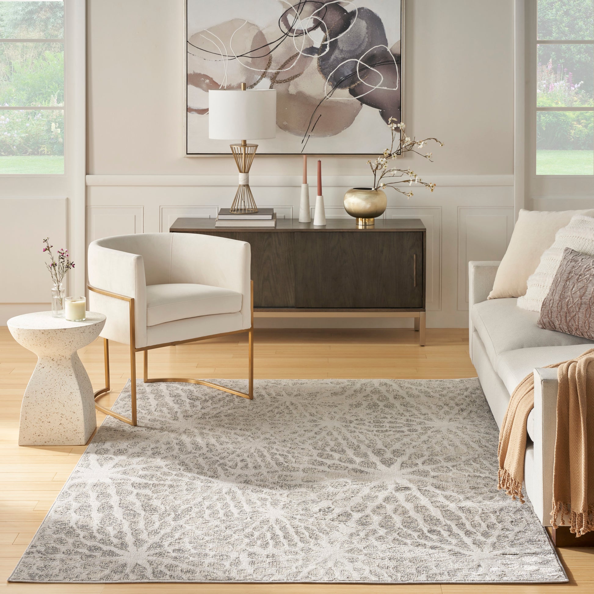 Neutral living room with a gray geometric patterned rug, white upholstered chair, wood console, and abstract wall art.