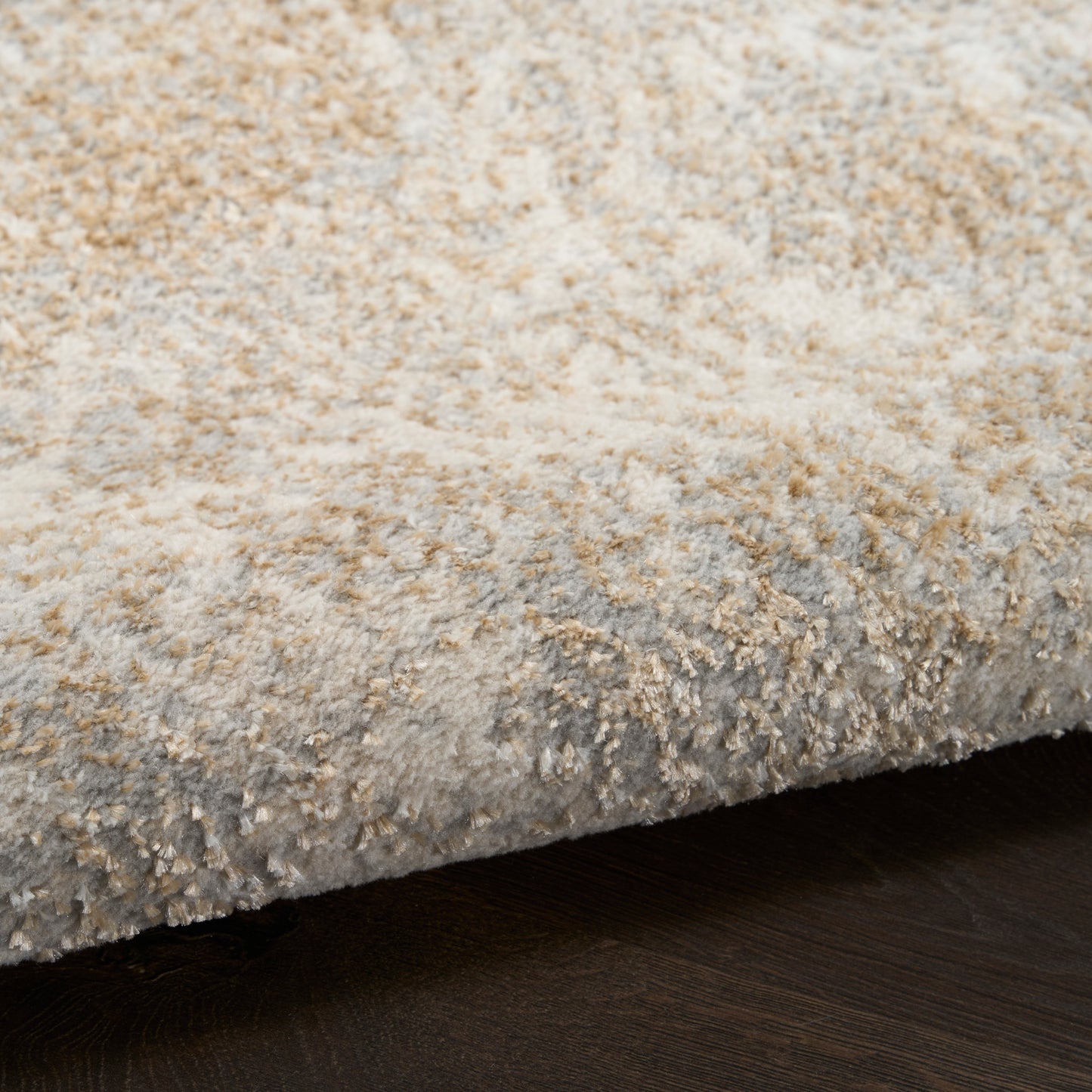 Close-up of a plush beige-gray textured area rug edge resting on a dark wood floor.