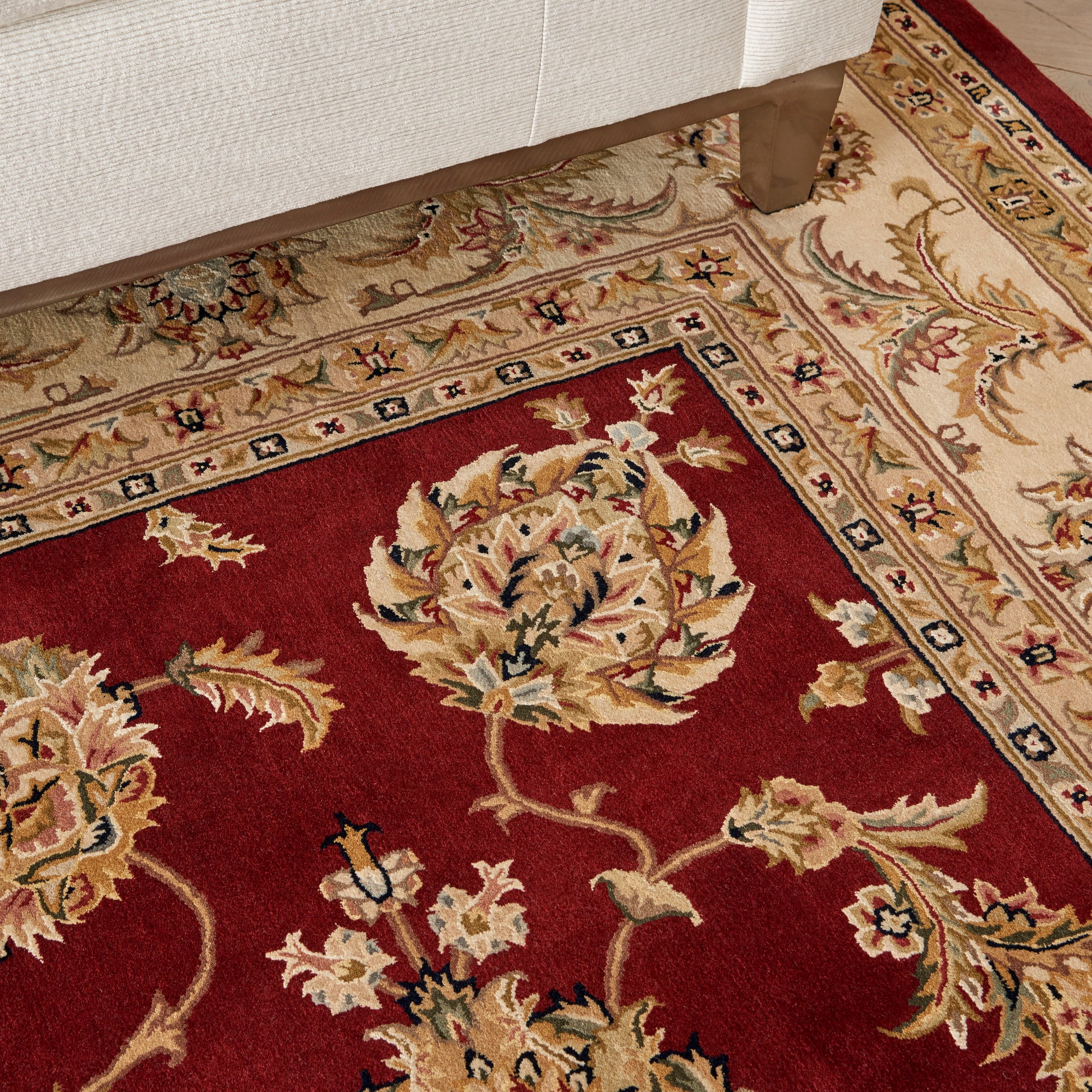 Red Persian-style floral area rug with cream, gold, and blue bouquets and a pale border; sofa leg nearby.