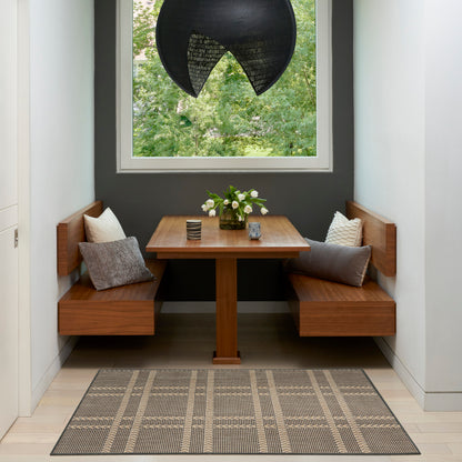Wood banquet nook with L-shaped benches, table, grey cushions, vase of white flowers, black curved pendant lamp, plaid rug.