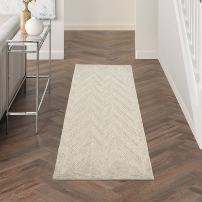 Beige chevron-patterned runner rug in a hallway with dark wood herringbone floor and a glass console table.