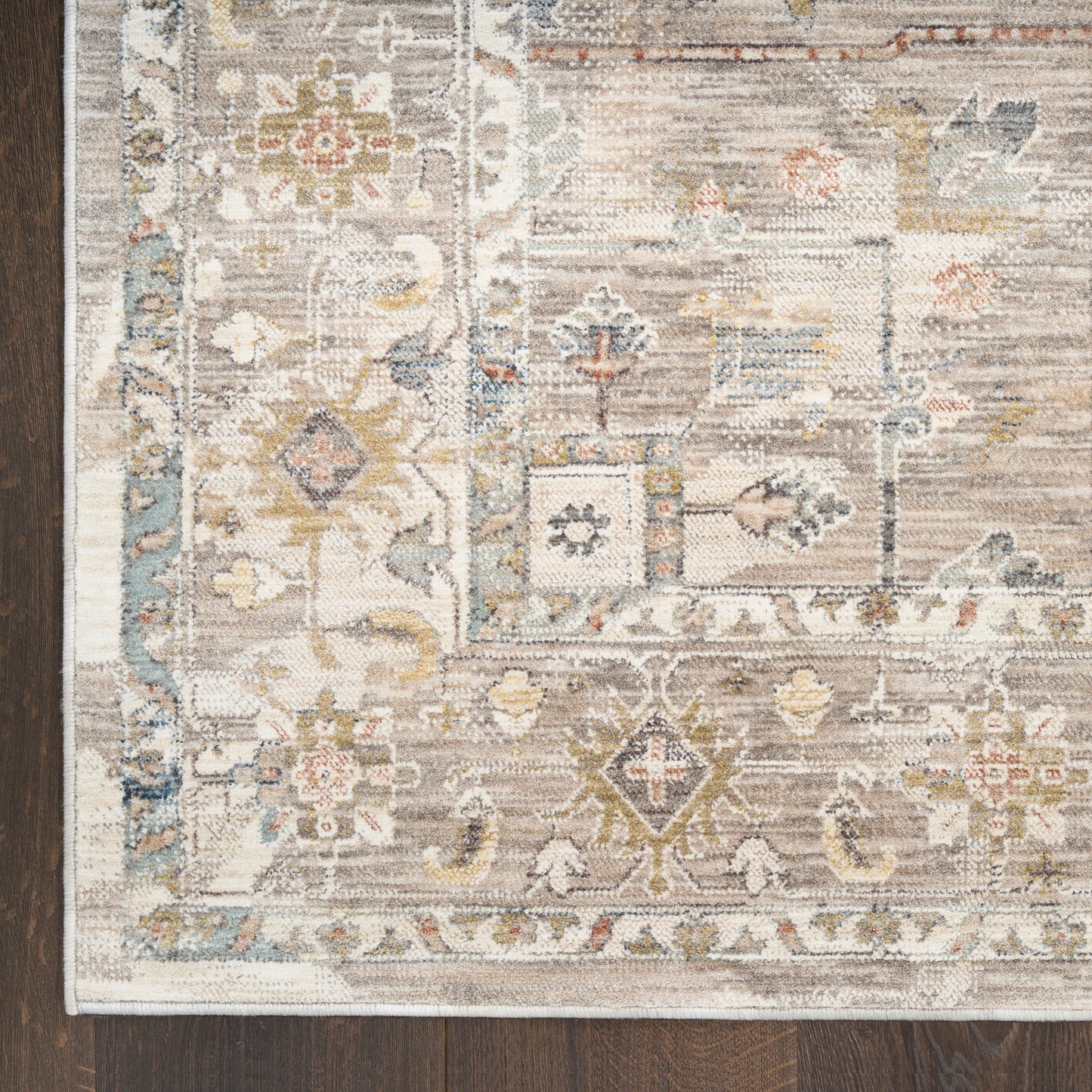 Corner of a vintage-style area rug with ivory, beige, blue & gold floral-geometric motifs on a dark wood floor.
