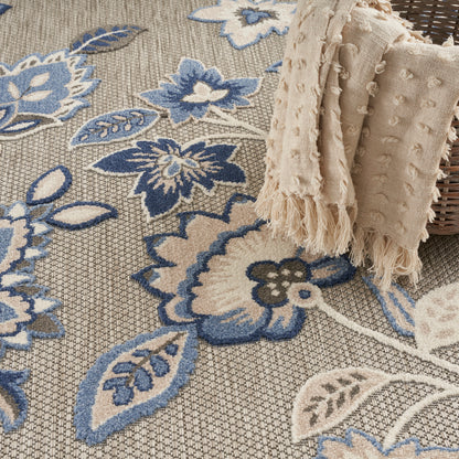 Beige woven rug with blue floral pattern, draped cream textured fringed throw over a wicker basket.