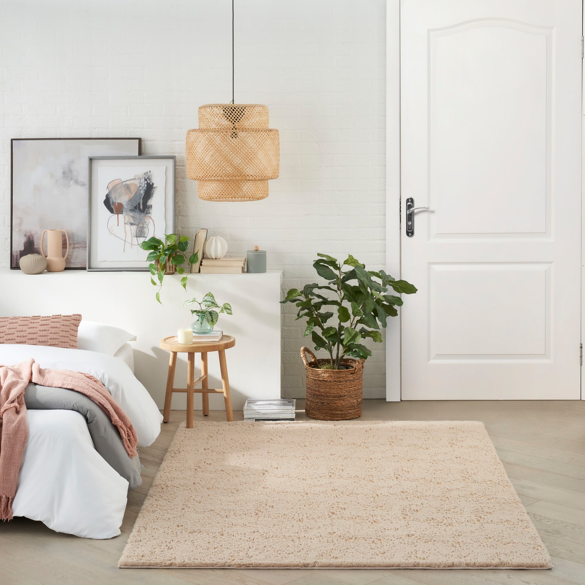 Bright modern bedroom with white walls, beige woven rug, wicker planter, rattan pendant light, framed art, white bed