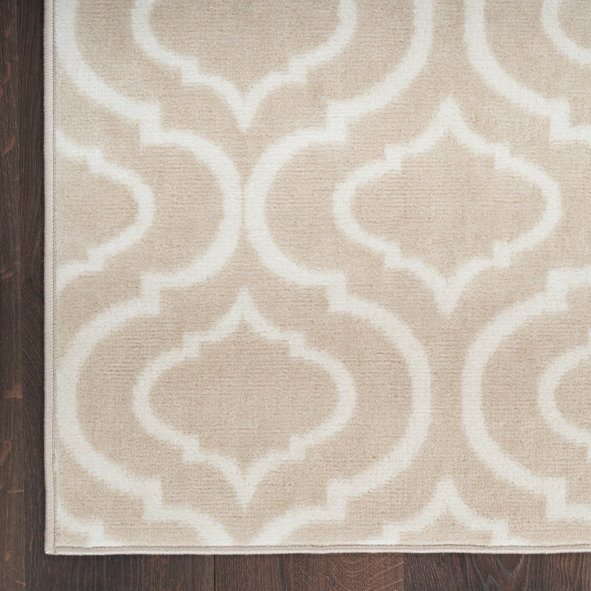 Beige rug with cream trellis pattern on dark wood floor; geometric oriental-inspired design.