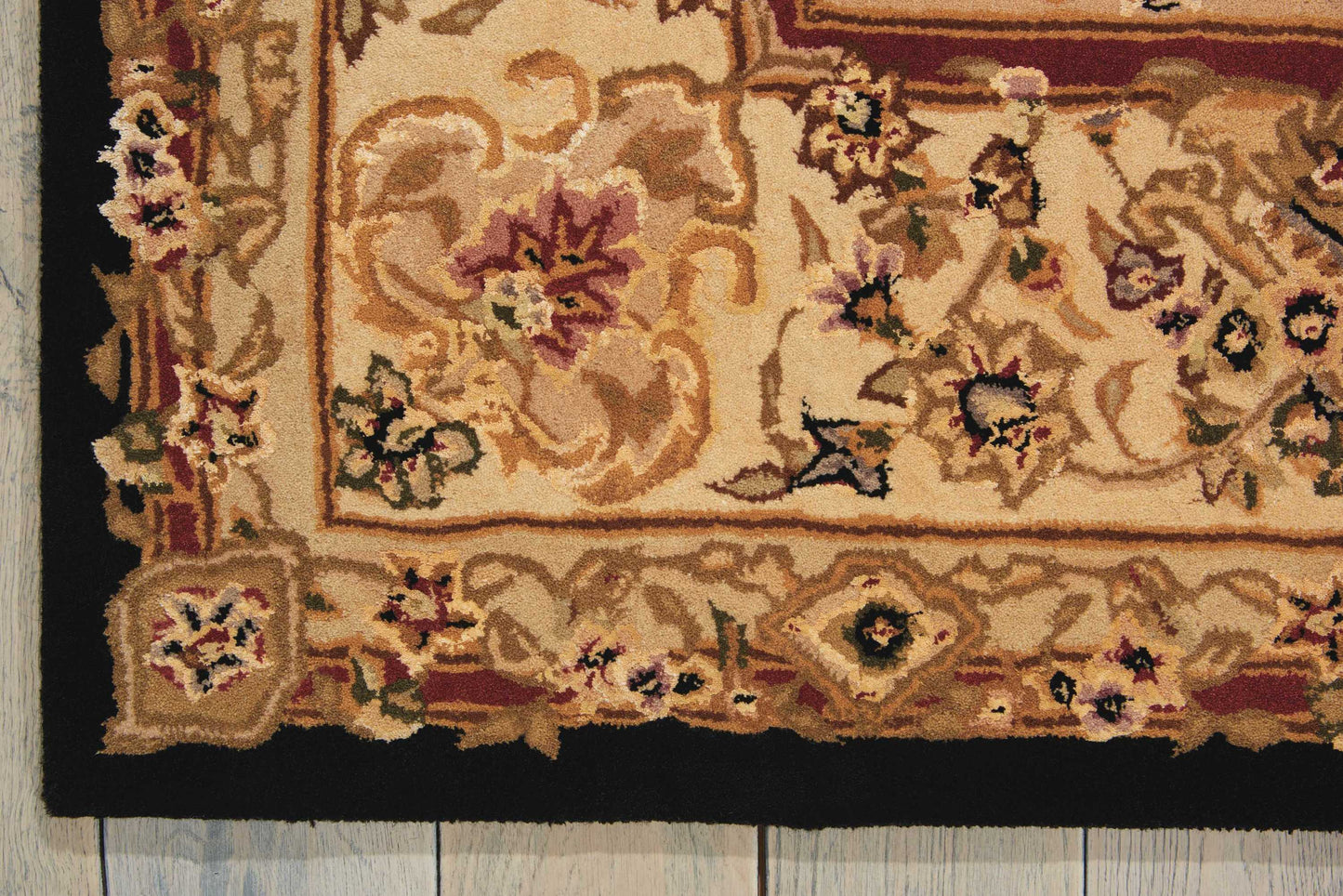 Beige oriental-style rug with floral motifs and burgundy border, tassel fringe, on wooden floor.