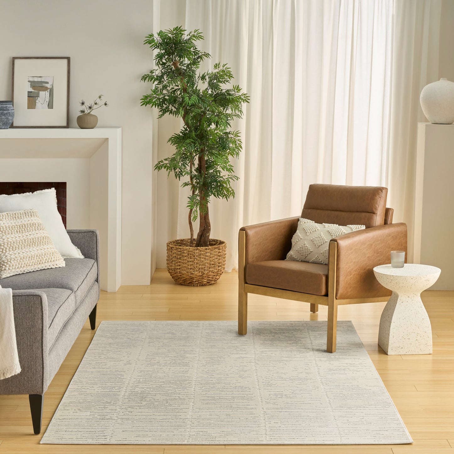 Light grey geometric area rug in a modern living room with a brown leather armchair, grey sofa, and potted plant.