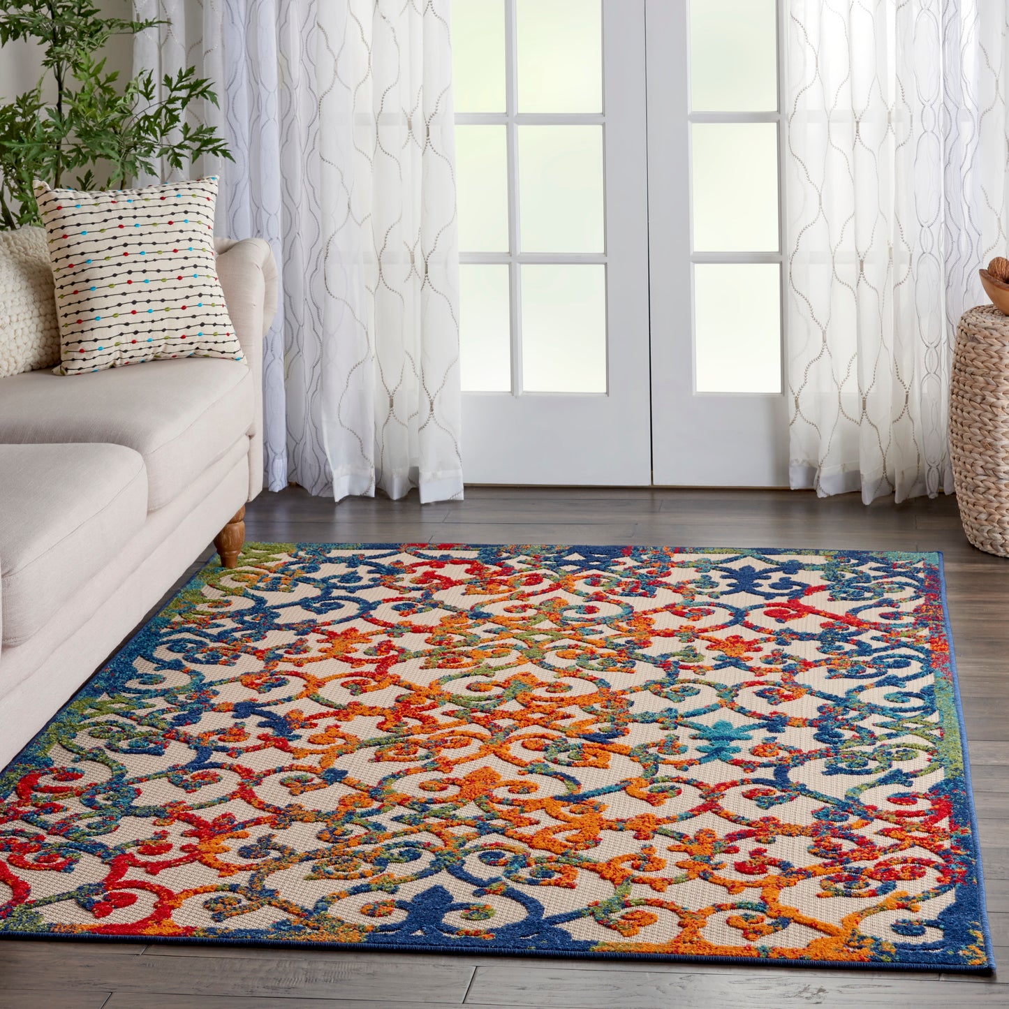 Rectangular area rug with a colorful floral-scroll pattern and blue border on a wood floor in a bright living room.
