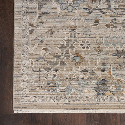 Beige oriental rug with blue-gray floral pattern, cream fringe along bottom, placed on dark wood floor.