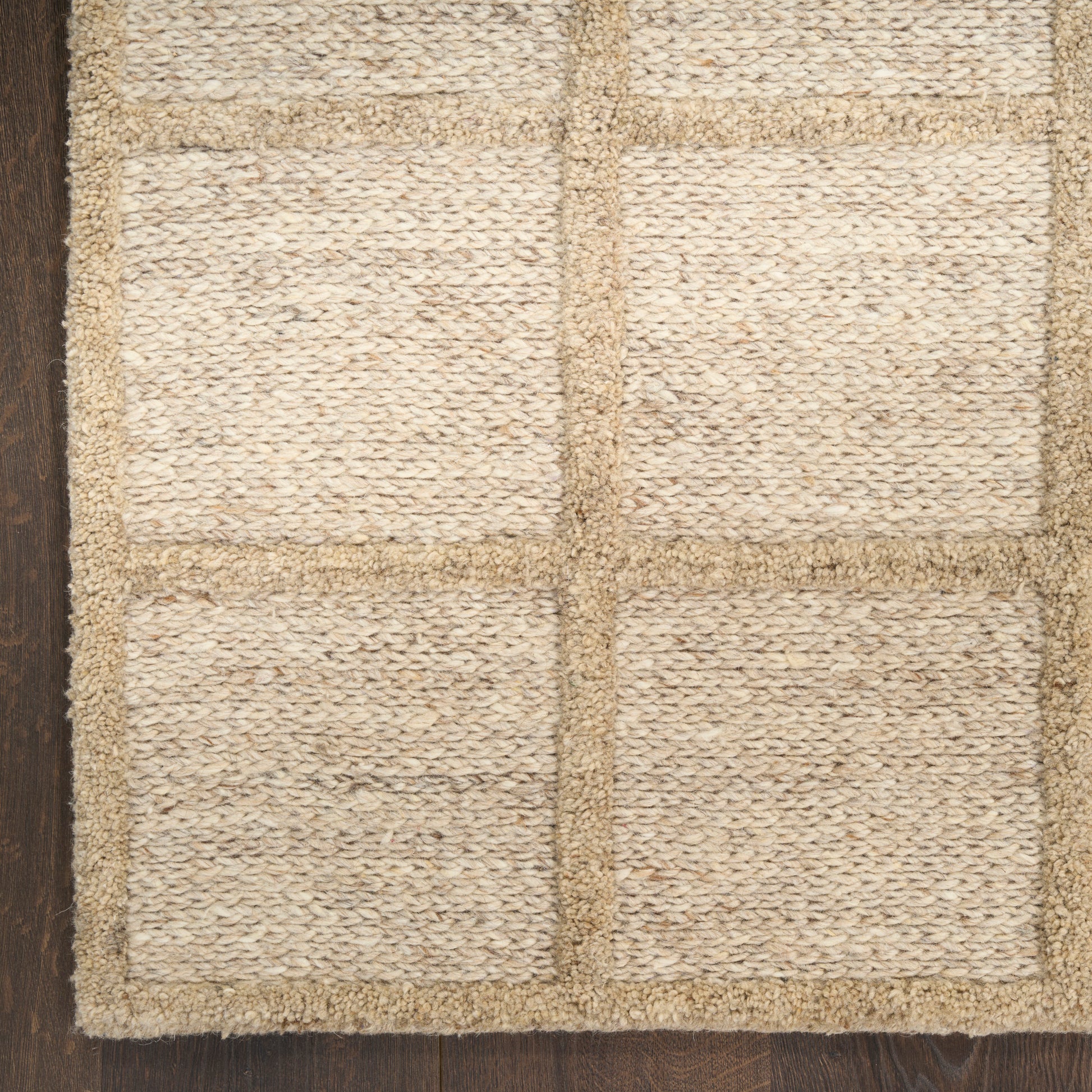 Beige woven jute rug with square panel grid on dark wood floor.