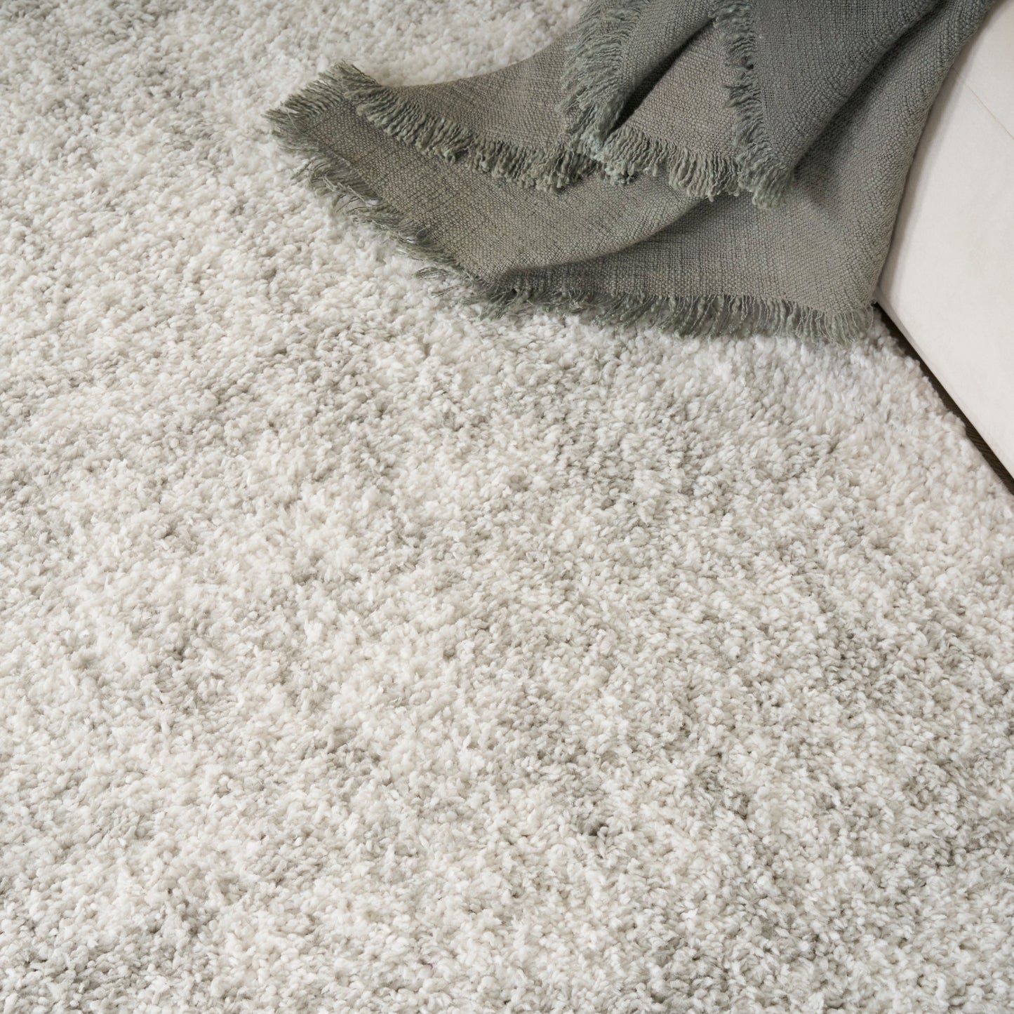Light gray shag carpet with a fringed gray throw blanket draped over a cream sofa.