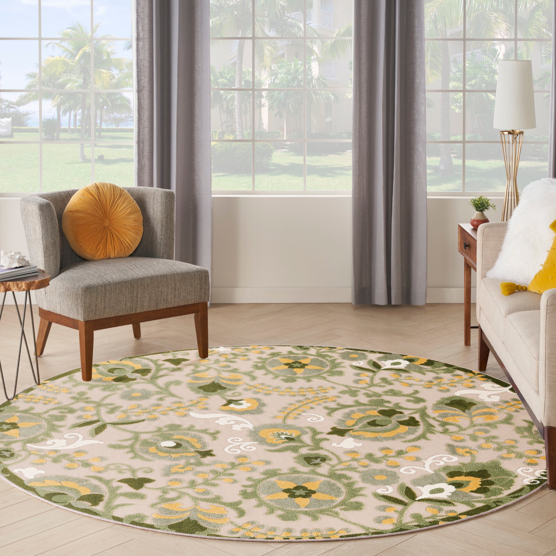Round woven area rug with green, yellow, and cream floral pattern on beige, in a bright living room.