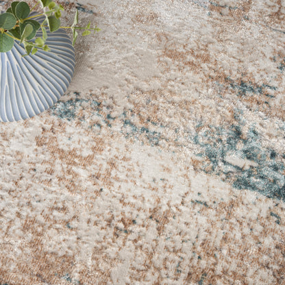 Blue pleated ceramic vase with green plant on a beige-blue patterned rug.