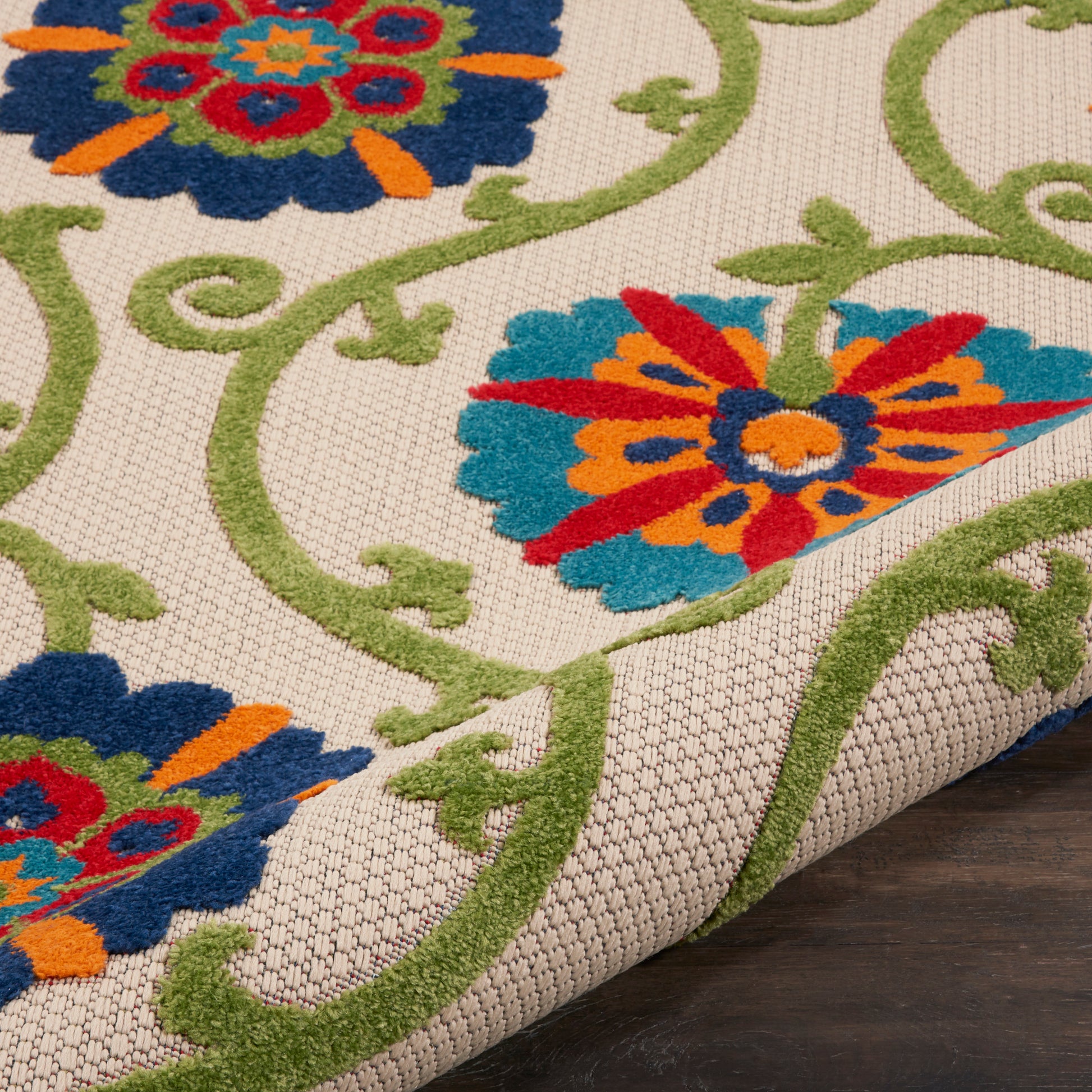 Beige woven rug with green scrolling vines and bold multicolor floral motifs in blue, red, orange, teal.