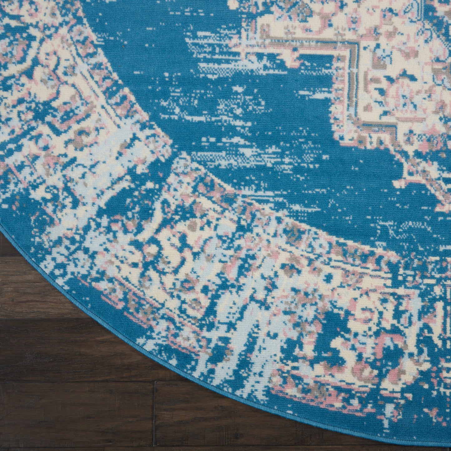 Round blue rug with pink & beige floral pattern on dark wood floor.