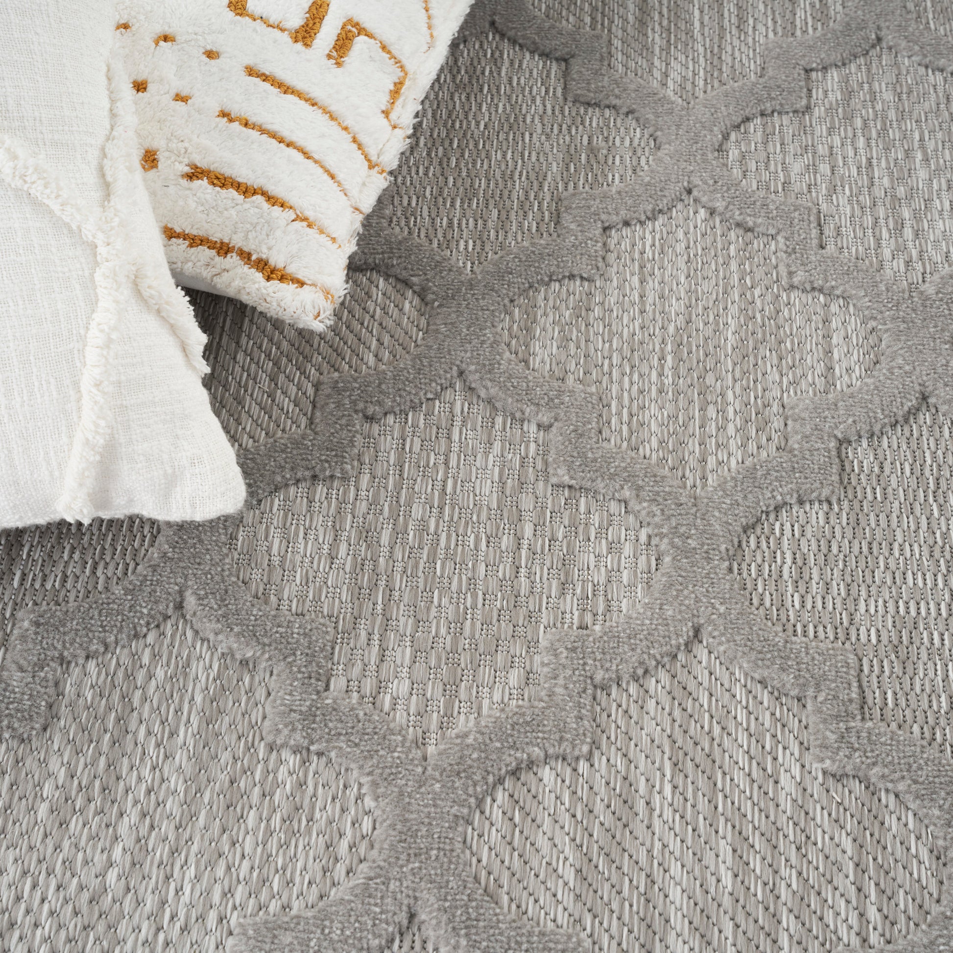 Gray textured rug with interlocking lattice pattern; white towel with orange stripes draped on edge.
