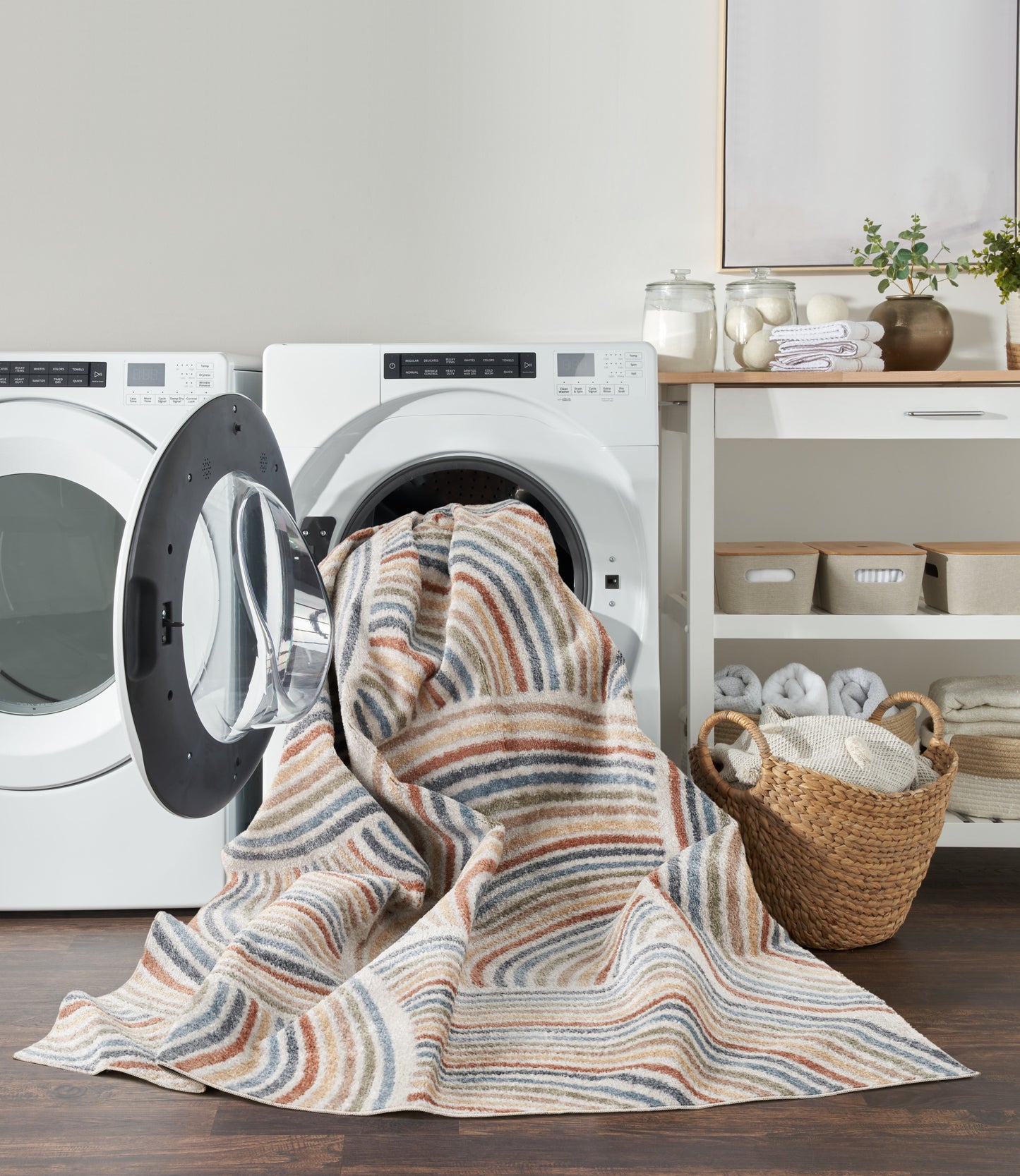 Striped woven cotton throw blanket in beige, blue and brown draped from an open front-loading washer in a cozy laundry room.