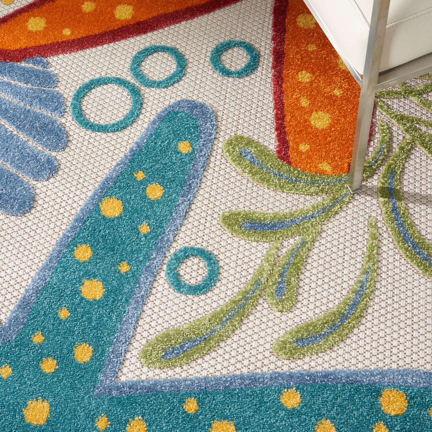 Close-up of a colorful round rug with turquoise blue shapes, yellow dots, teal rings, orange border, and green leaf patterns.